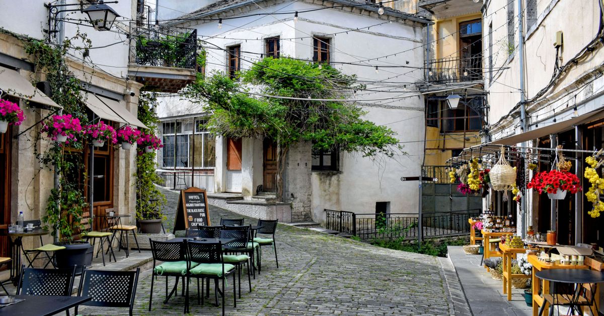 Discover a picturesque street in Gjirokastër, Albania, featuring cozy outdoor cafes and vibrant plants.